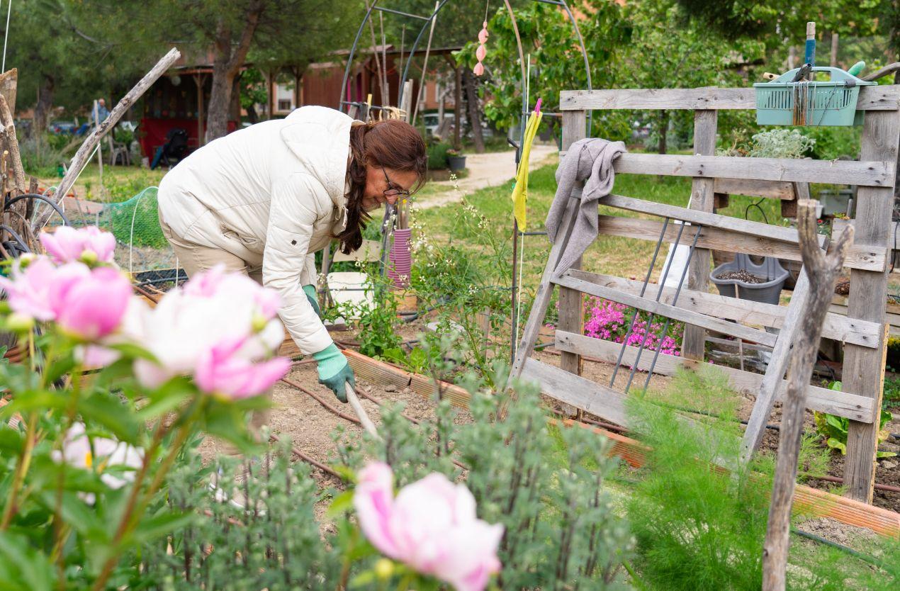 Eine Frau arbeitet in einem nachhaltigen Garten mit recyceltem Holz und natürlichen Materialien. Im Hintergrund sorgen Ziersteine und Pflanzen für eine umweltfreundliche Gestaltung.